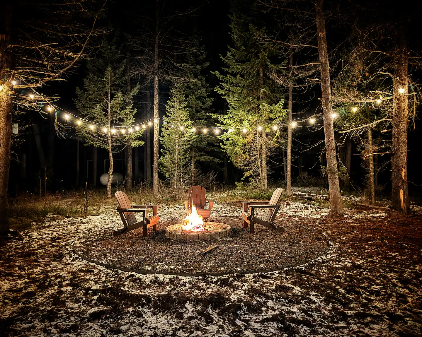 Firepit with Adirondack chairs under string lights at night